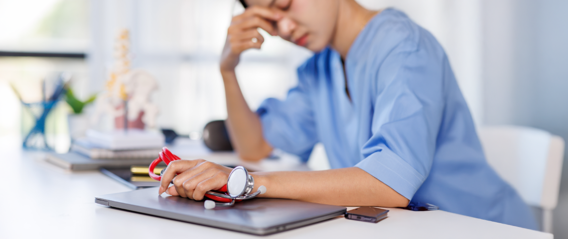Nurse sits at desk holding a red stethoscope.