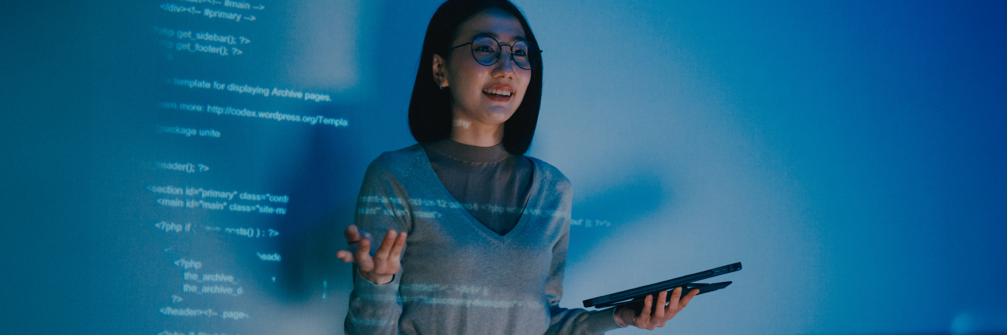 Woman in a gray sweater presents in front of coding language.
