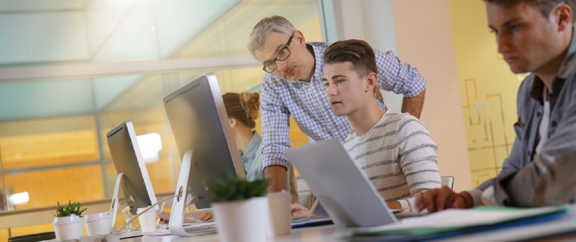 Group of students in a computer lab being helped by a teacher.