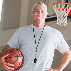 Coach standing by a basketball hoop wearing a whistle and holding the ball