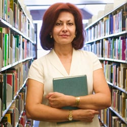 Educator standing between two library bookshelves and holding books