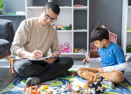 School counselor writing down notes while child plays with toys