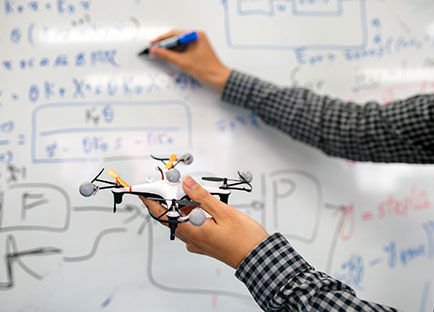 Hands holding drone and writing equations on whiteboard